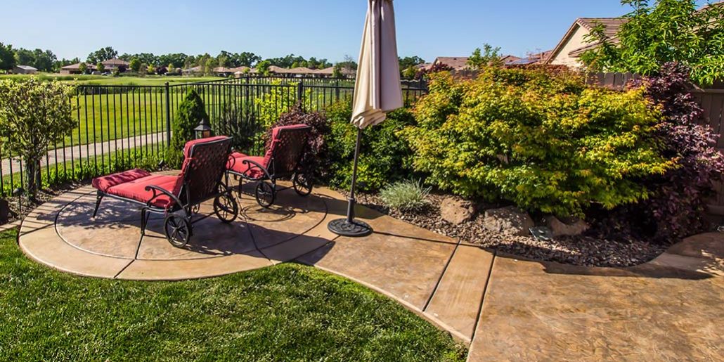 Lounge Chairs Overlooking Green Field Blue Pond Stamped Concrete Patios
